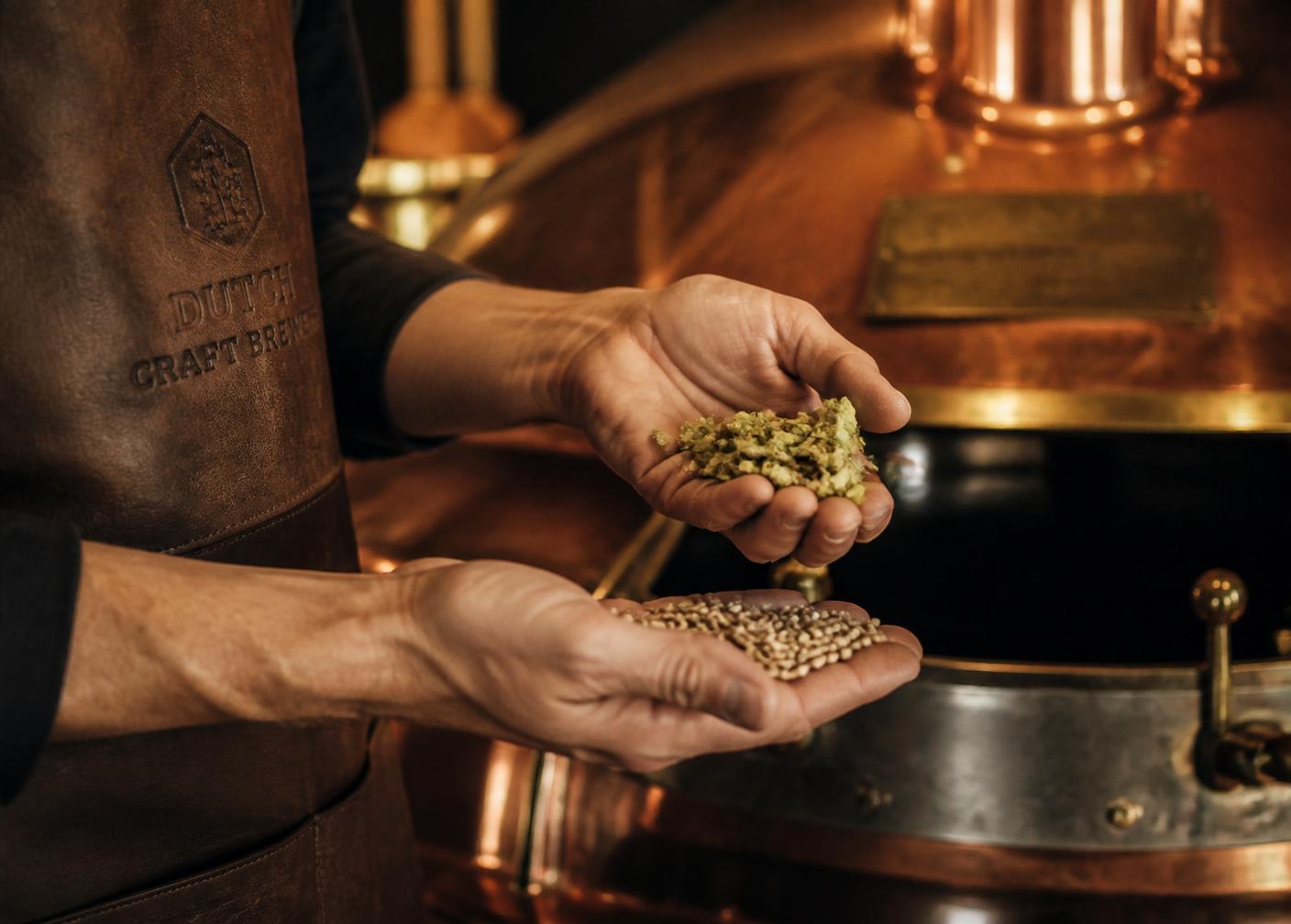 Brouwershanden met hop en mout bij een koperen ketel